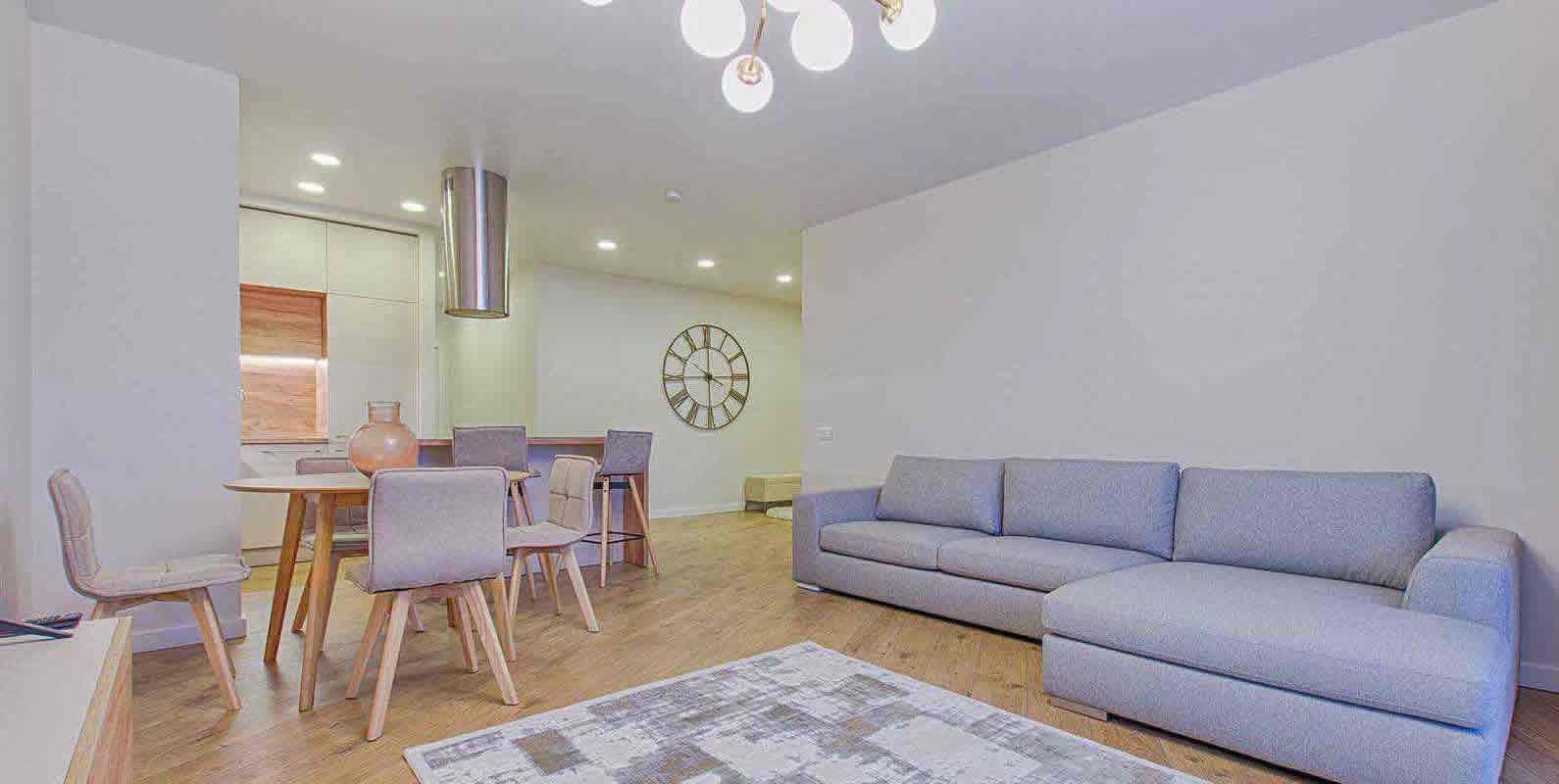 A modern living room with a gray sectional sofa, a dining area with a round table and chairs, and stylish lighting fixtures, creating a cozy and elegant ambiance.