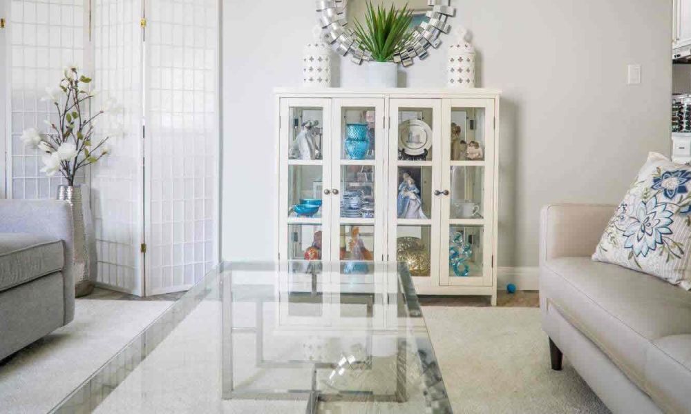 A living room with a glass coffee table, a white display cabinet with decorative items, and a comfortable sofa, exuding a fresh and elegant feel.