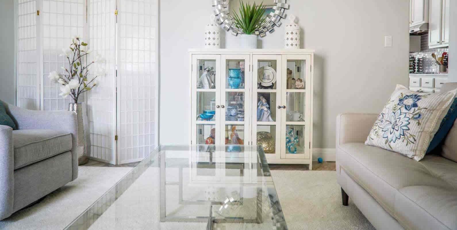 A living room with a glass coffee table, a white display cabinet with decorative items, and a comfortable sofa, exuding a fresh and elegant feel.